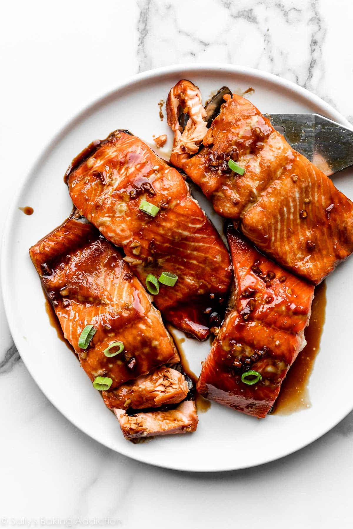 4 baked salmon filets on white plate smothered in a dark honey soy glaze and sprinkled with green onion.