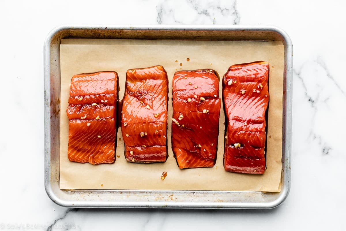 4 filetes de salmón marinados en una bandeja para hornear pequeña forrada con papel pergamino.