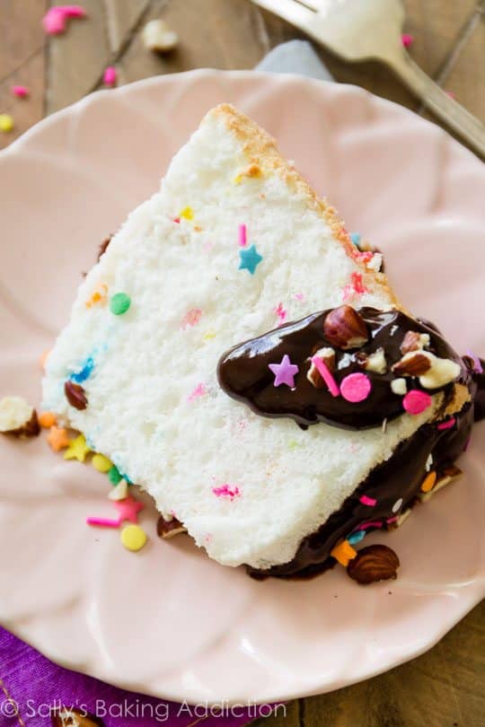 slice of sprinkle angel food cake with chocolate ganache on a pink plate