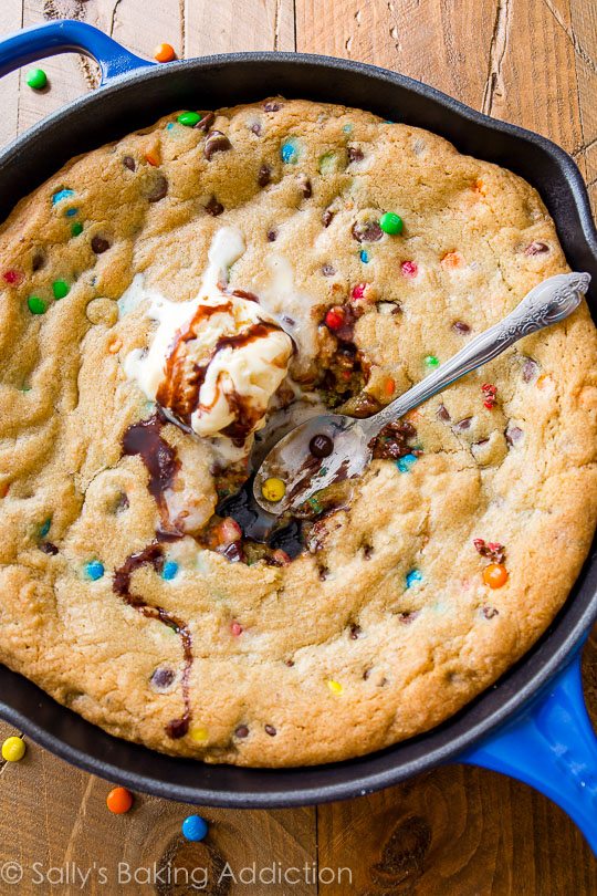 M&Ms chocolate chip skillet cookie topped with ice cream in a blue skillet with a spoon