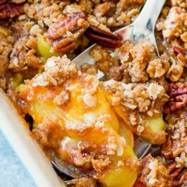 peach pecan crisp in a baking dish with a serving spoon