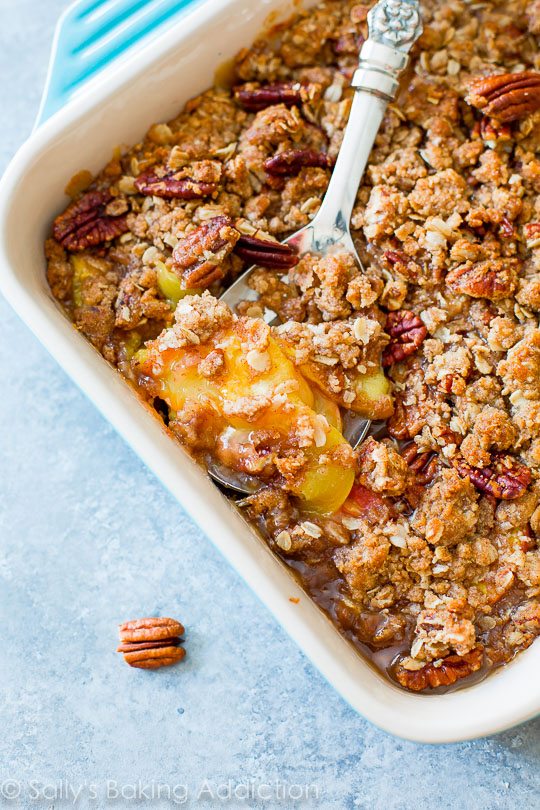 peach pecan crisp in a baking dish with a serving spoon
