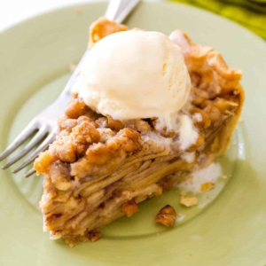 slice of apple crumble pie with a scoop of vanilla ice cream on a light green plate with a fork