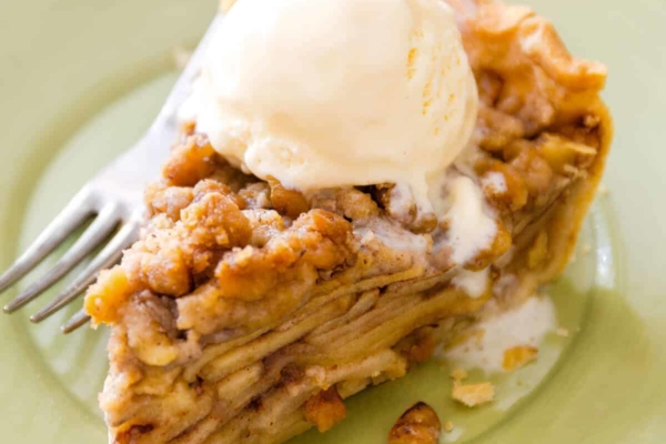 slice of apple crumble pie with a scoop of vanilla ice cream on a light green plate with a fork