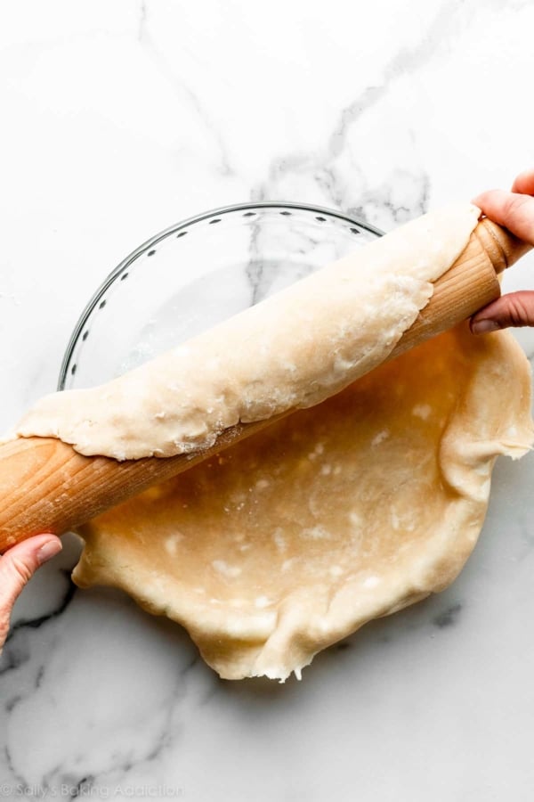 hands using rolling pin to fit pie crust over glass pie dish.