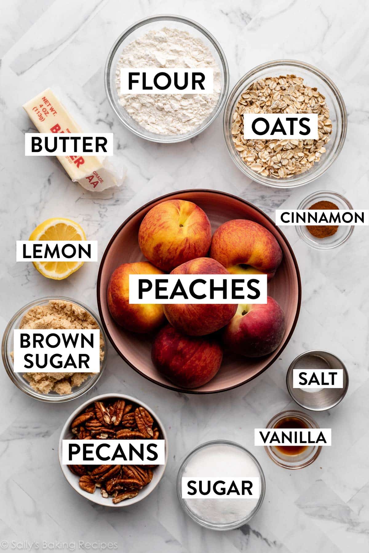 ingredients on marble counter including peaches, oats, flour, butter, lemon pecans, and sugar.
