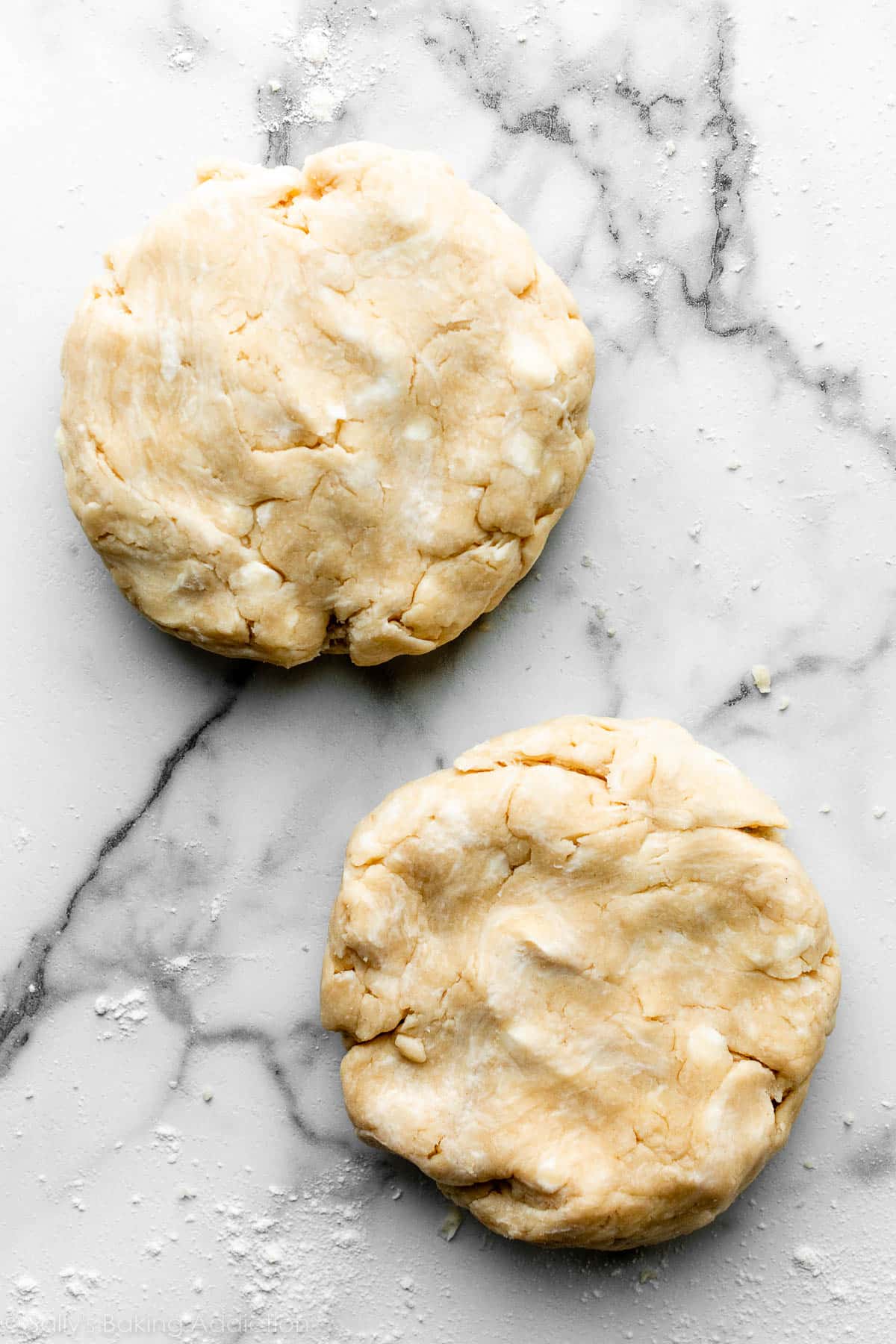 overhead photo of two discs of pie dough on a marble countertop.