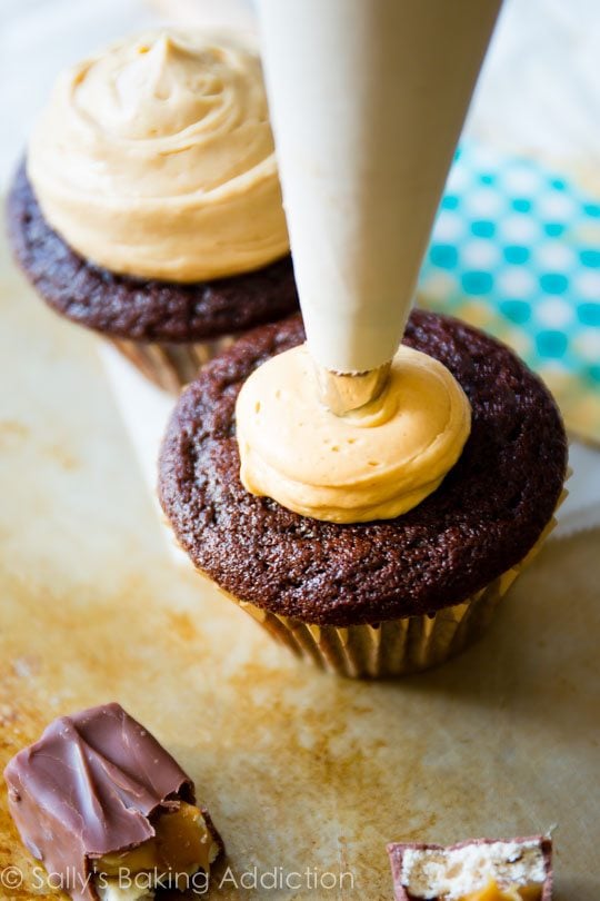 piping peanut butter frosting onto chocolate cupcakes
