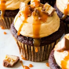 chocolate cupcakes topped with peanut butter frosting, chopped Snickers candy bars, and salted caramel