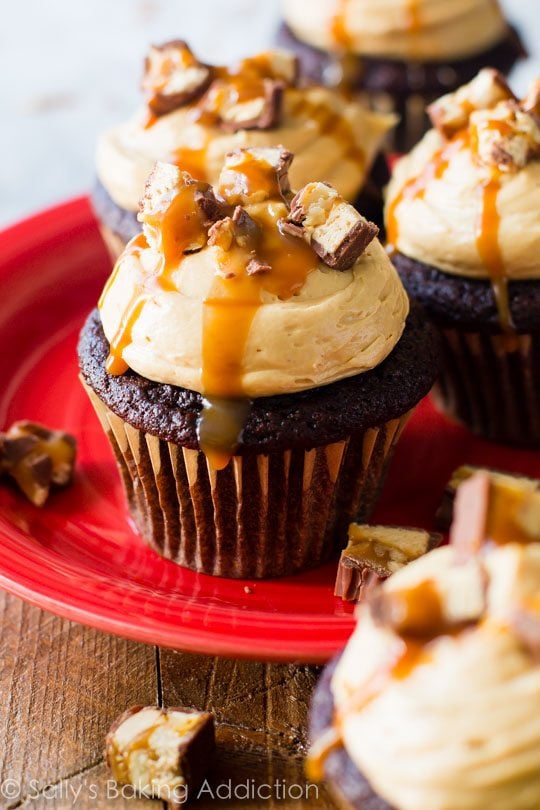 chocolate cupcakes topped with peanut butter frosting, chopped Snickers candy bars, and salted caramel on a red plate