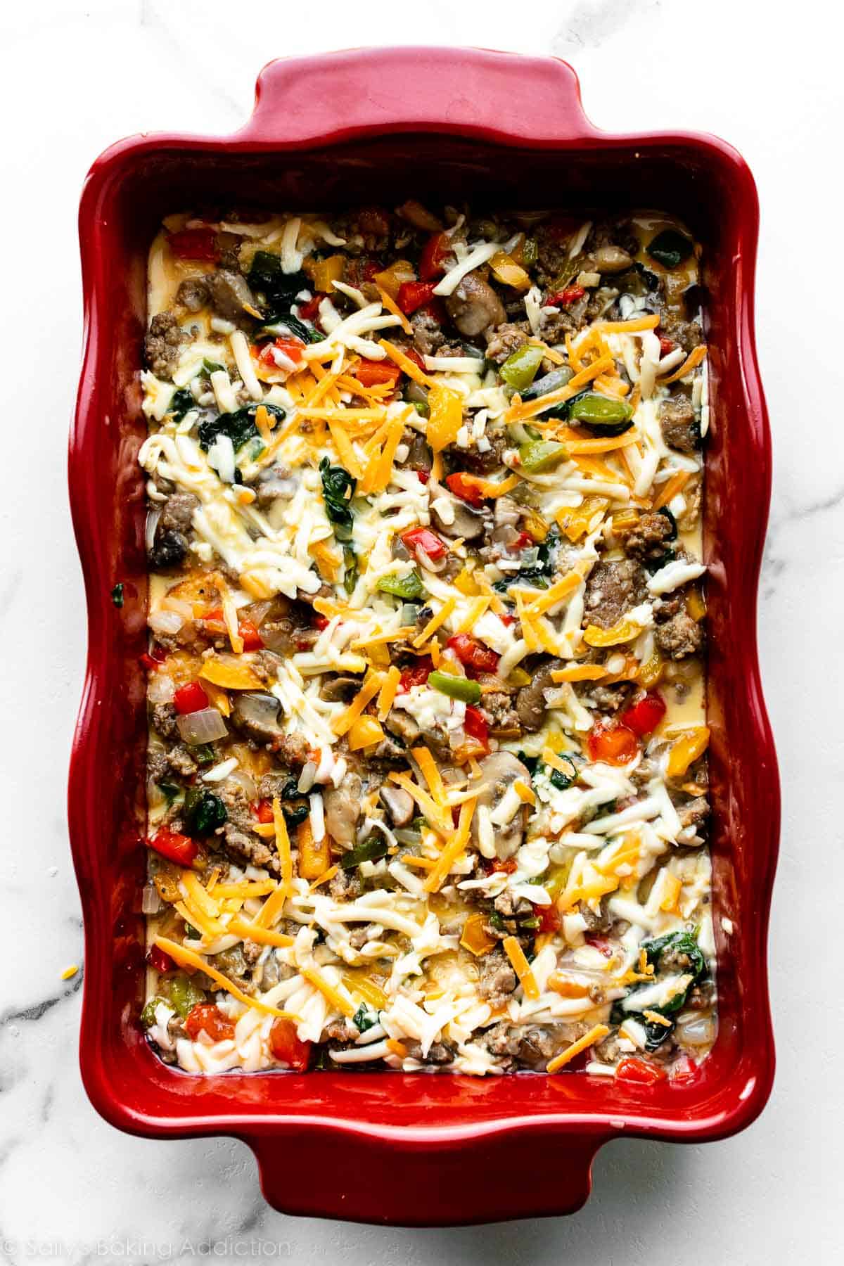 egg, vegetables, cheese, sausage, and bread combination in casserole dish on marble counter.