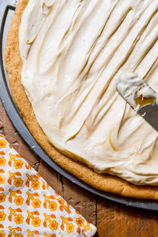 spreading caramel cream cheese frosting onto snickerdoodle cookie crust