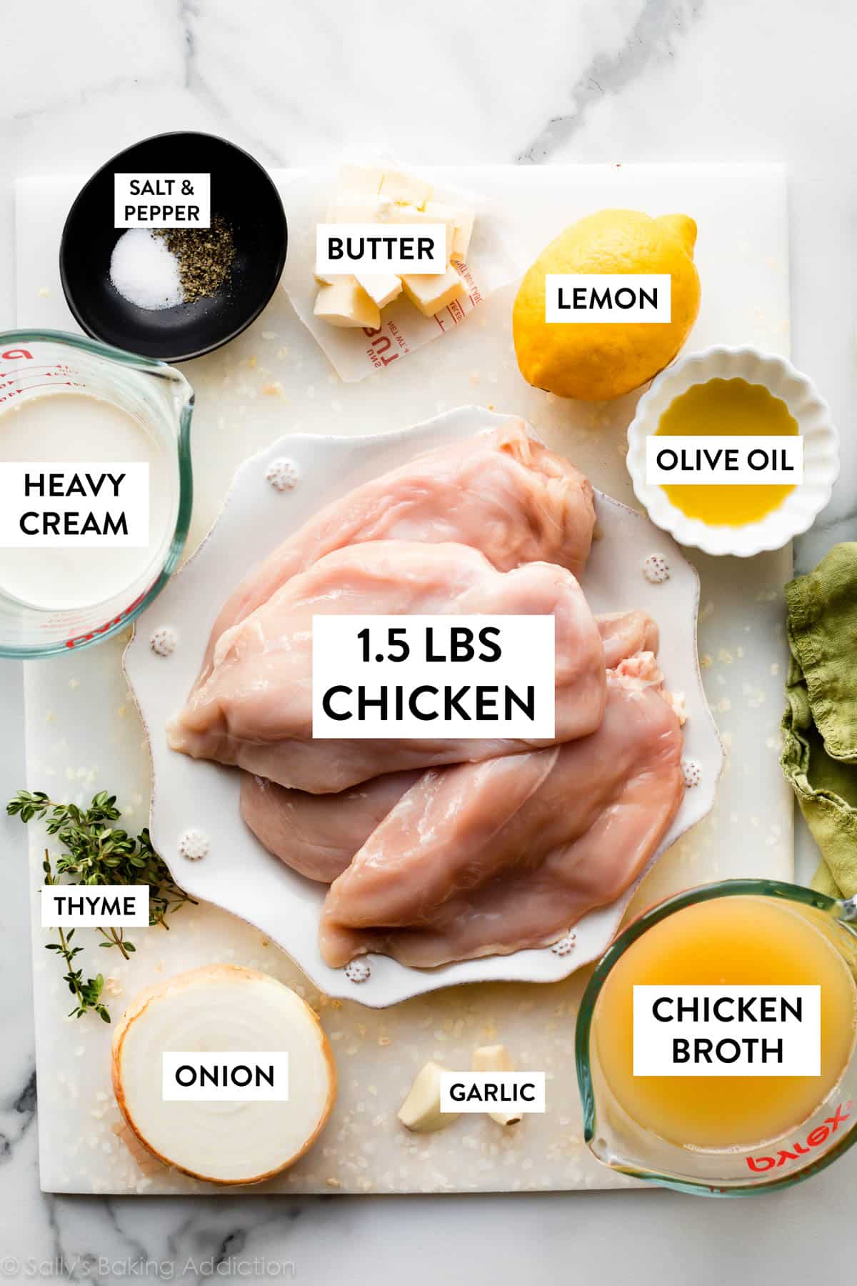 Ingredienti in ciotole e sul piatto tra cui petto di pollo crudo, limone, olio d'oliva, burro, brodo di pollo e timo