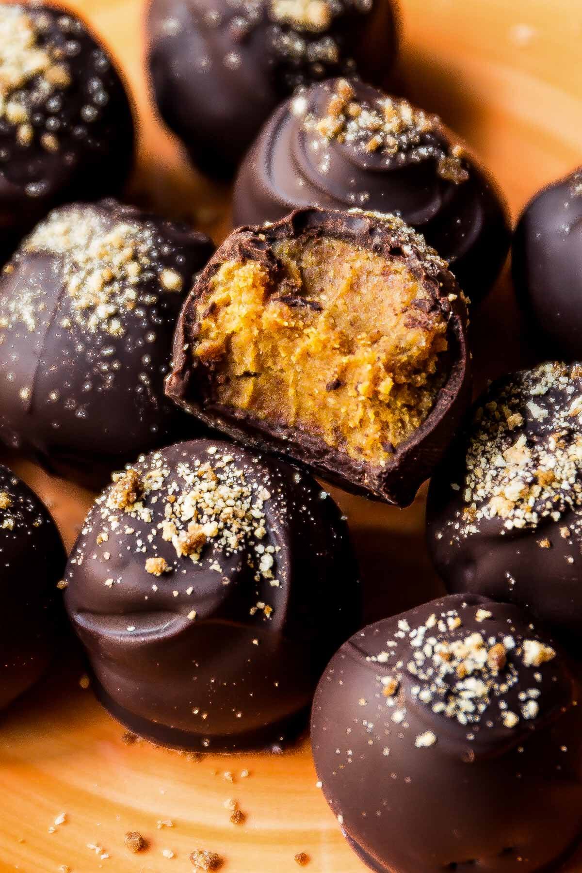 pumpkin spice truffles coated in dark chocolate and a bite taken out of one showing the truffle filling
