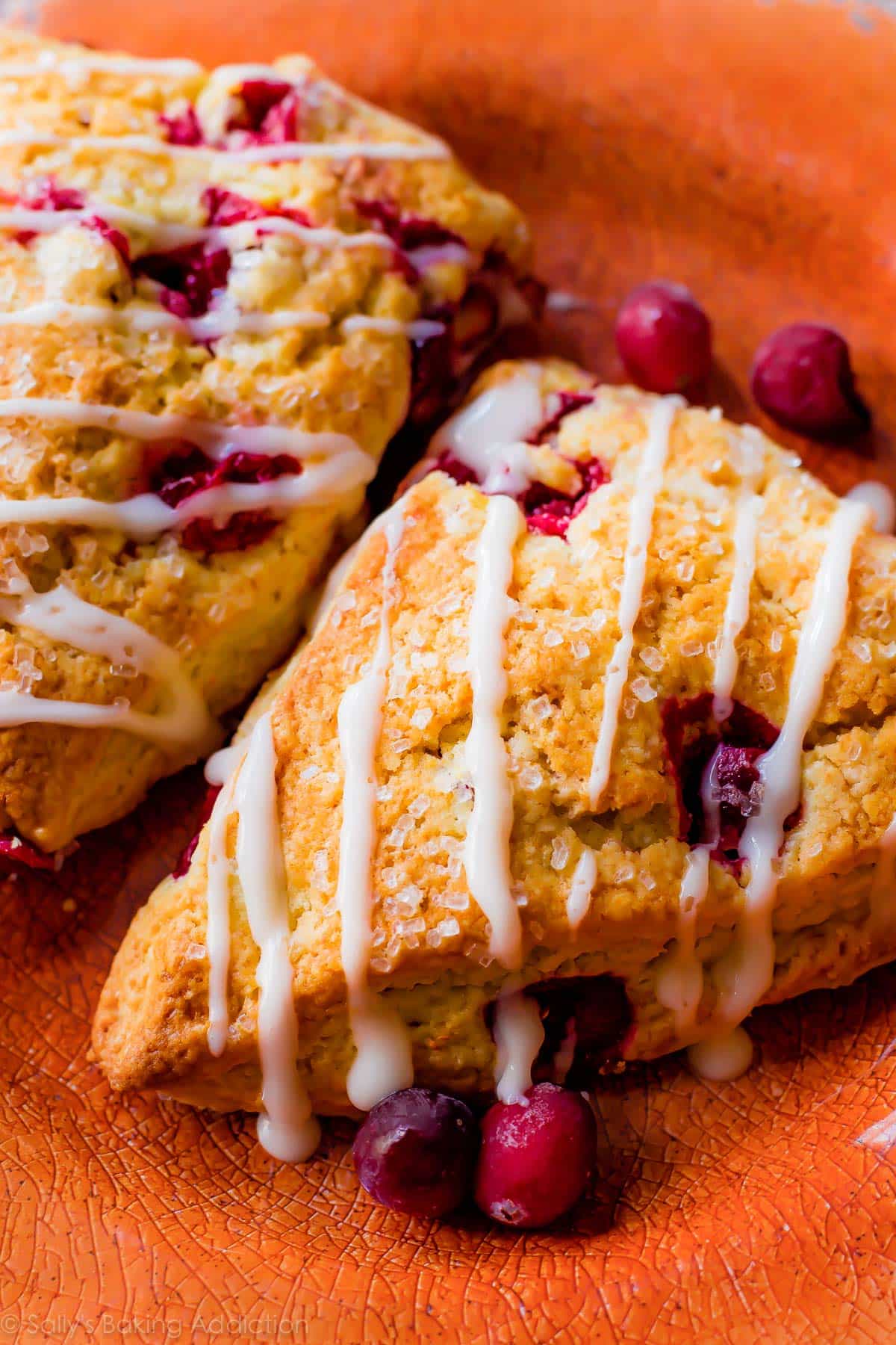 cranberry orange scones with icing on an orange plate