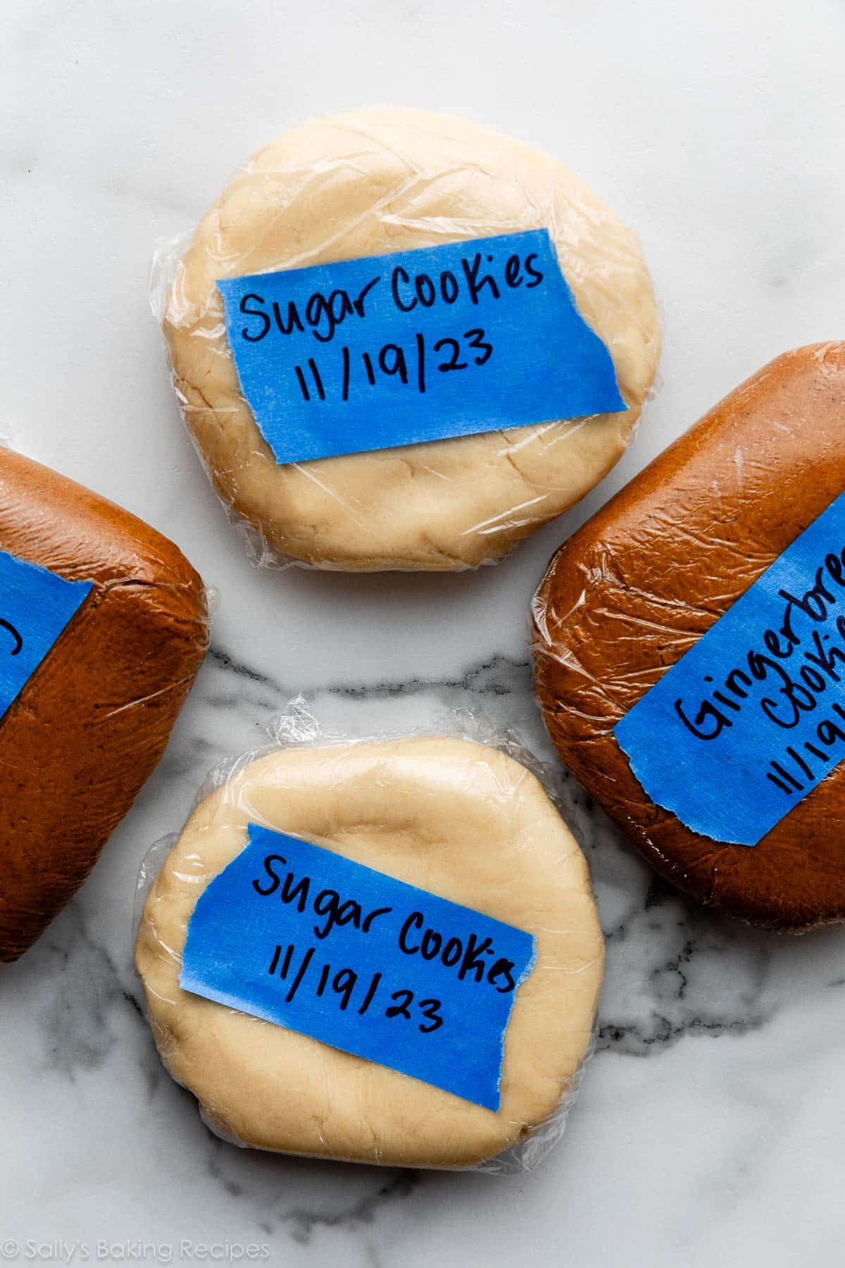 sugar cookie dough and gingerbread cookie dough discs wrapped in plastic wrap and labeled with blue tape.