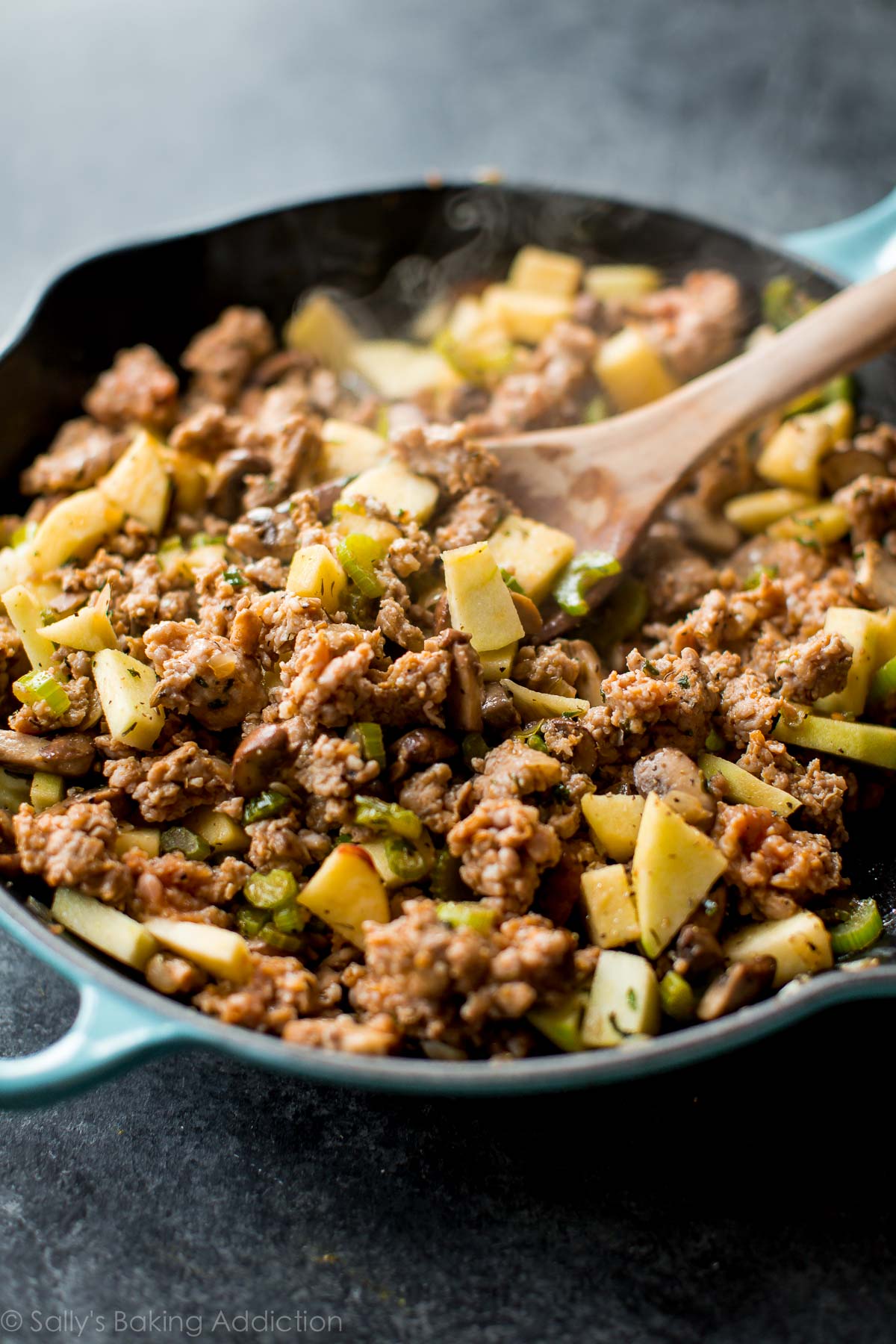 sausage with herbs and apples in a skillet with a wood spoon