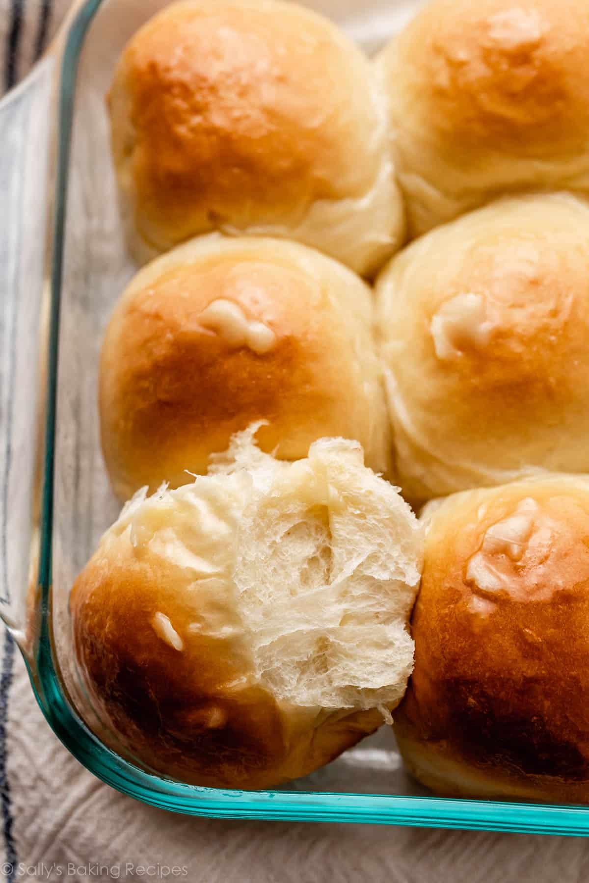honey butter rolls in glass baking dish with one turned on its side to show flakiness.