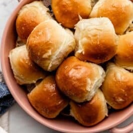 dinner rolls with honey butter topping in pink ceramic pie dish.