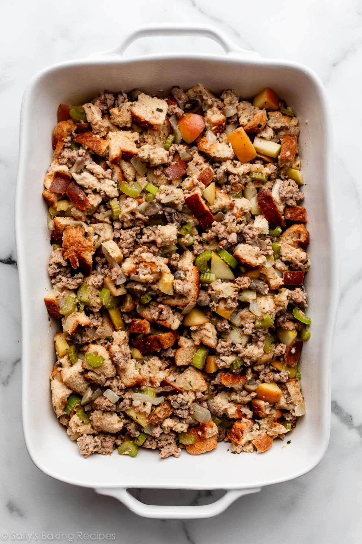 sausage herb bread stuffing with celery and apples in white baking dish before baking.