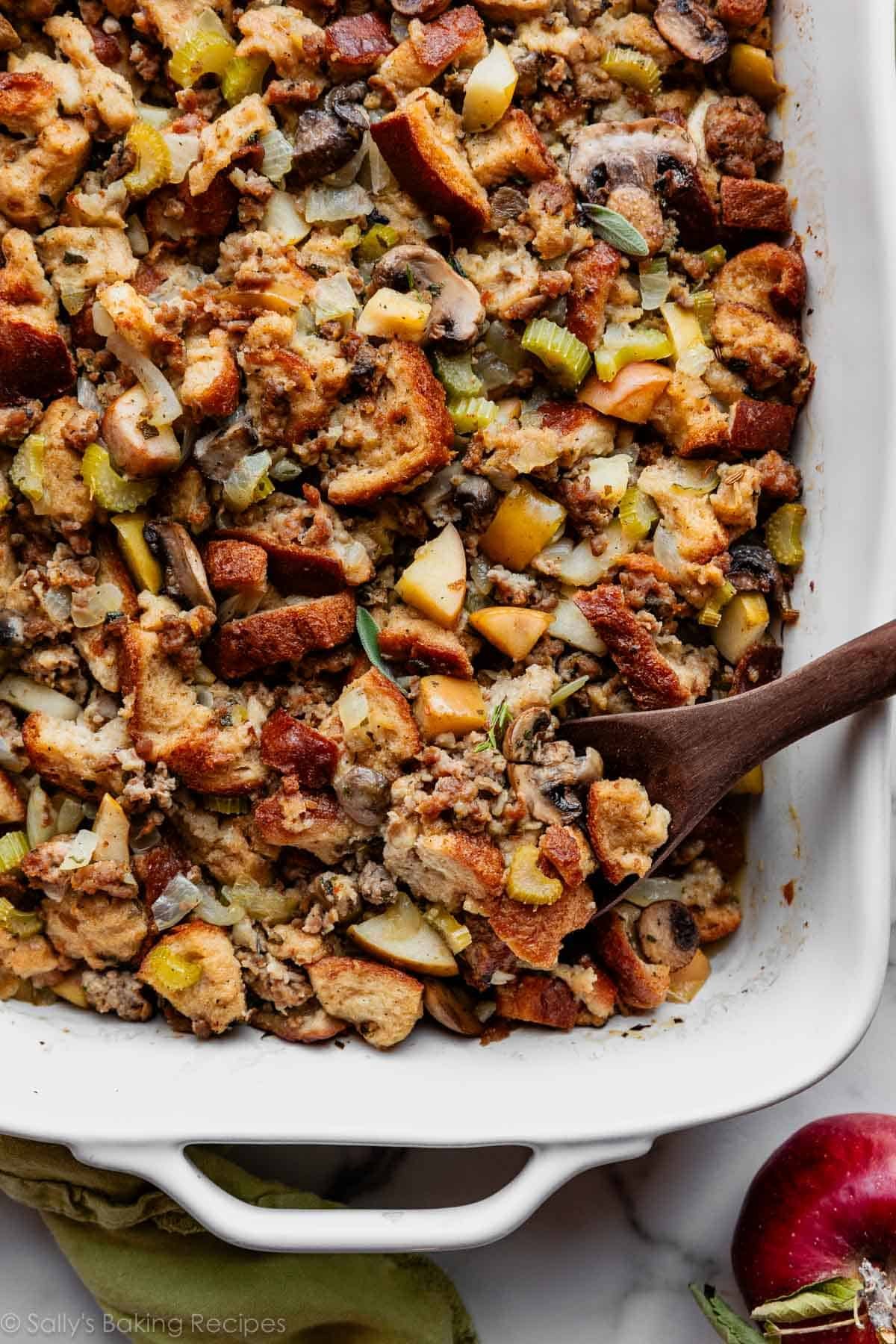 sausage herb Thanksgiving stuffing in a white baking dish with wooden spoon.