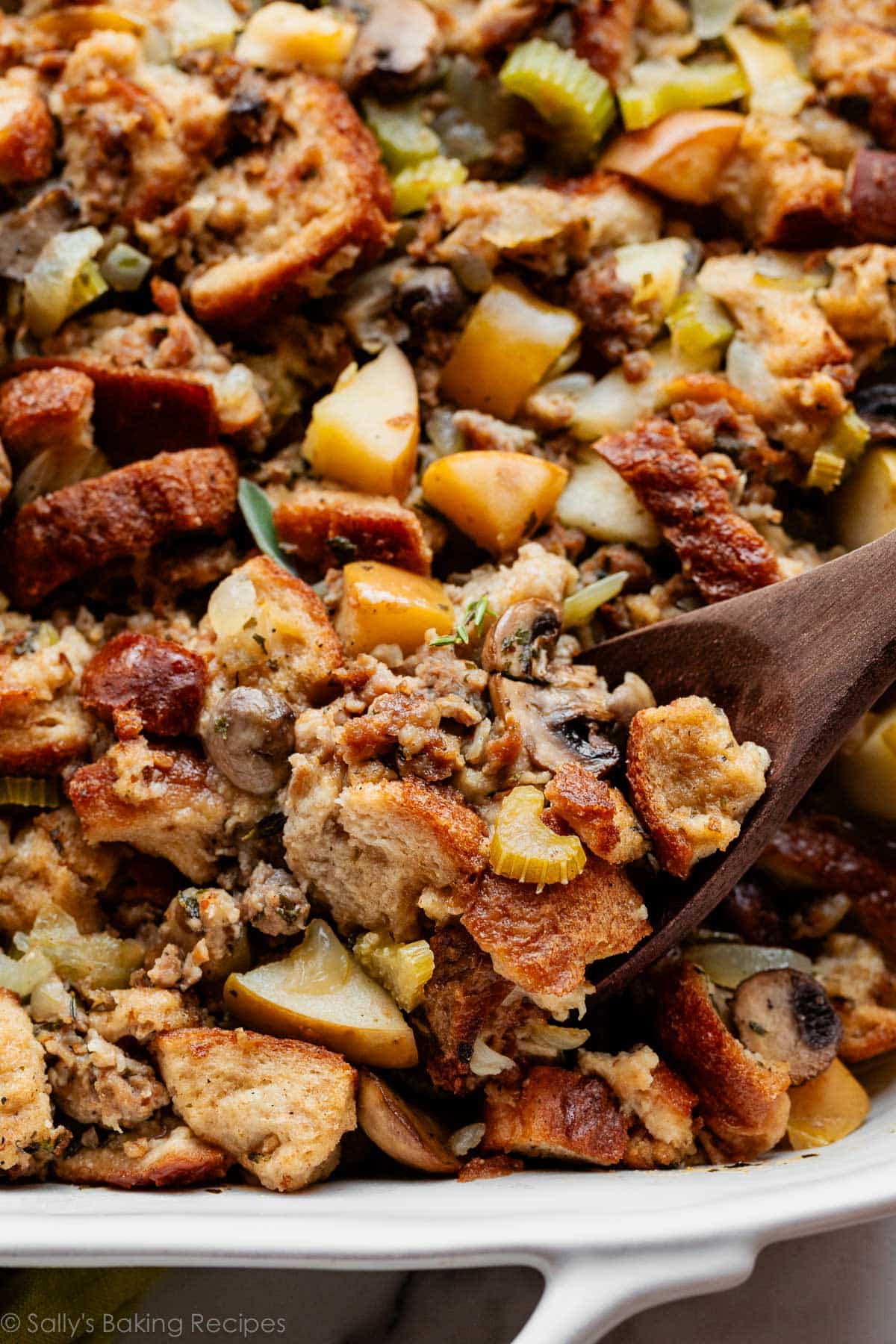 wooden spoon serving a spoonful of sausage herb apple Thanksgiving stuffing.