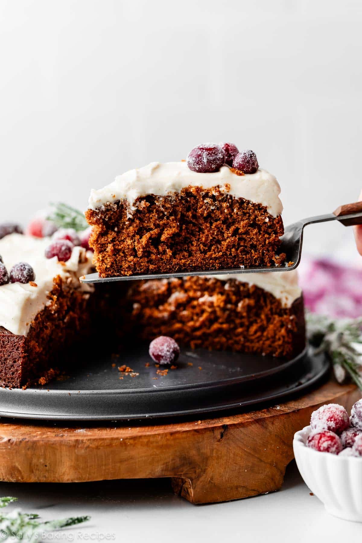 slice of gingerbread cake with cream cheese frosting being held up with a cake server.