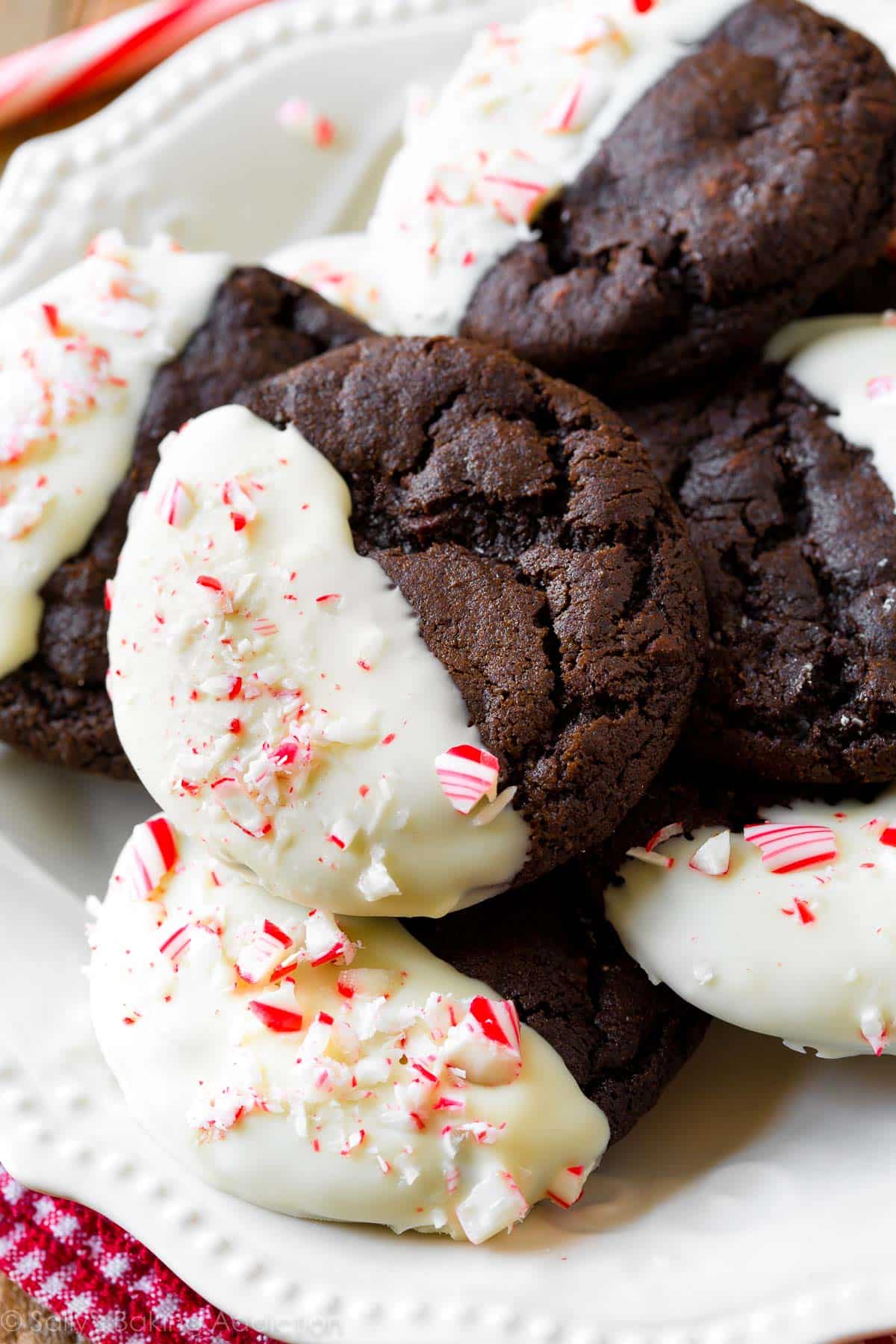 peppermint mocha cookies with half of each cookie dipped in white chocolate and topped with crushed candy canes on a white plate