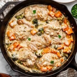 cooked chicken and vegetables in a creamy garlic sauce in a black cast iron skillet.