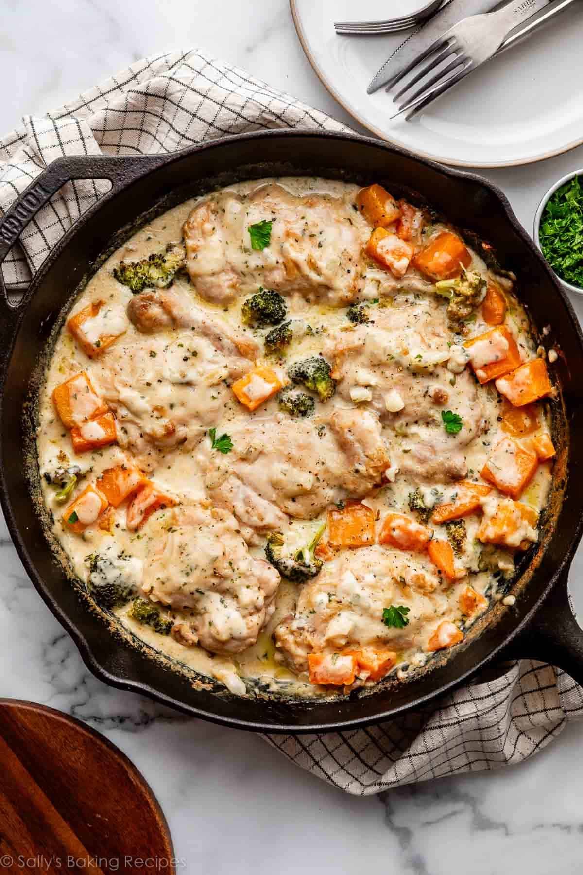 cooked chicken and vegetables in a creamy garlic sauce in a black cast iron skillet.
