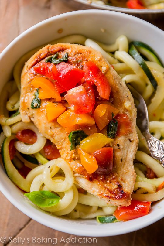 zucchini noodles and chicken breast with tomatoes on top in a white bowl