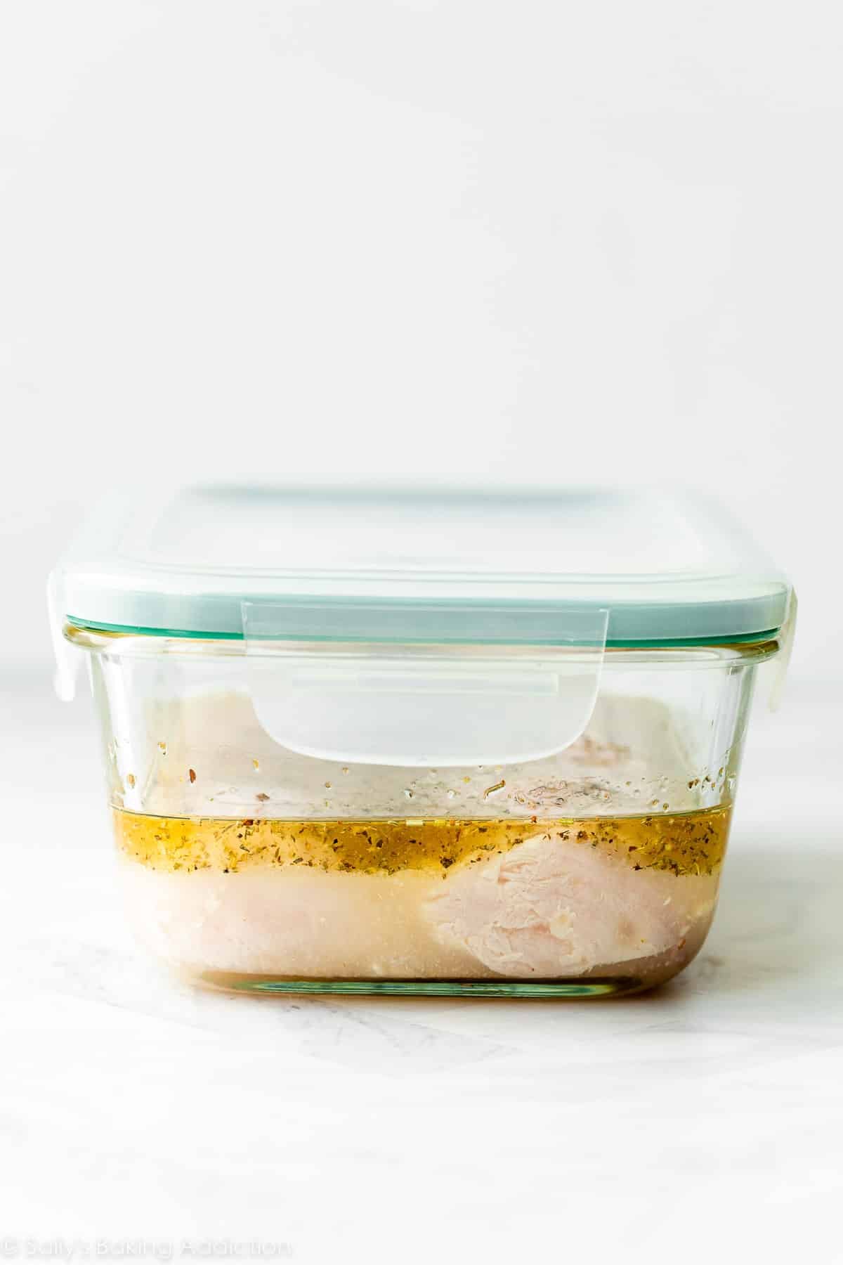 chicken marinating in Italian dressing in glass container with lid.