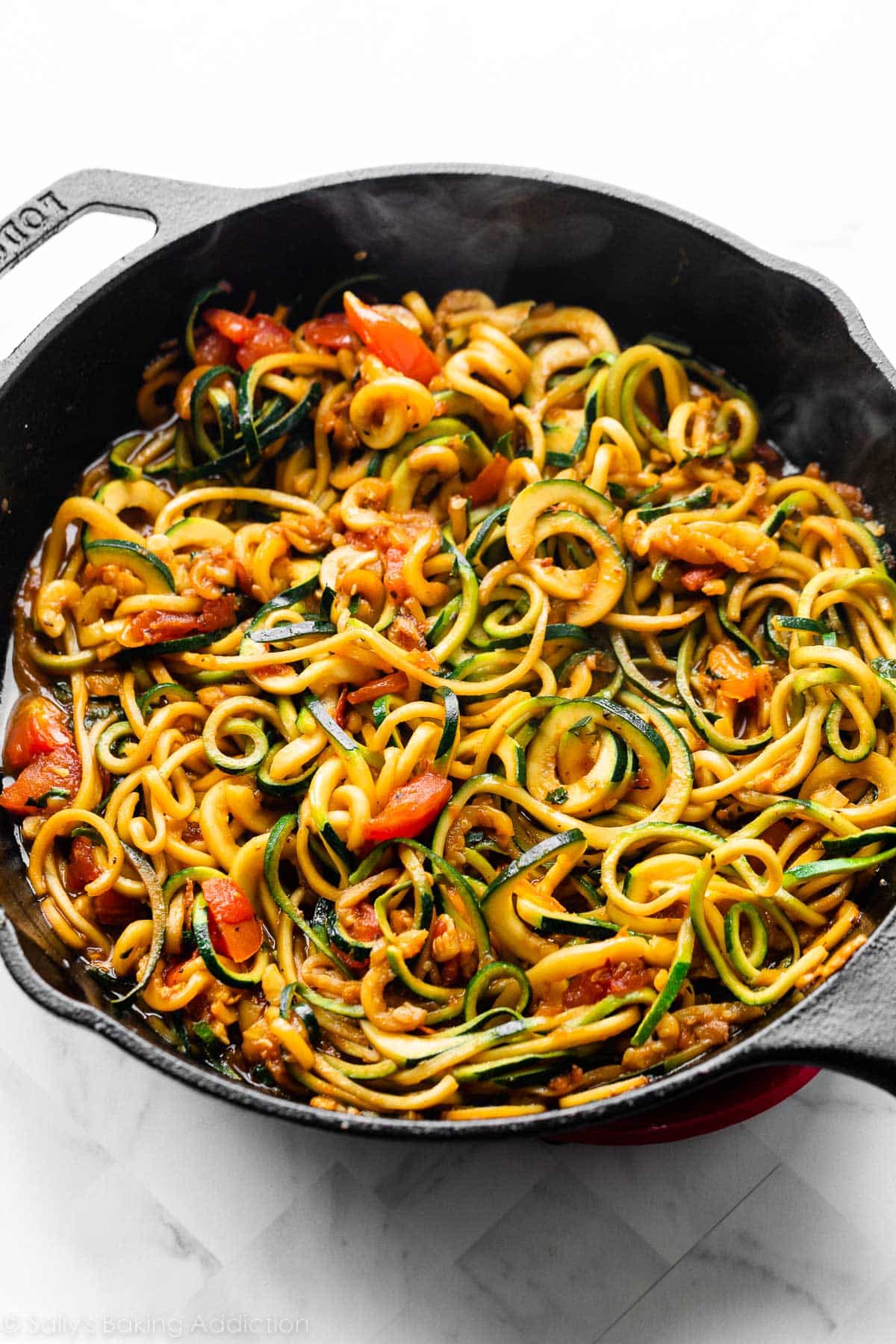 heated zucchini noodles in cast iron skillet with tomatoes and garlic.