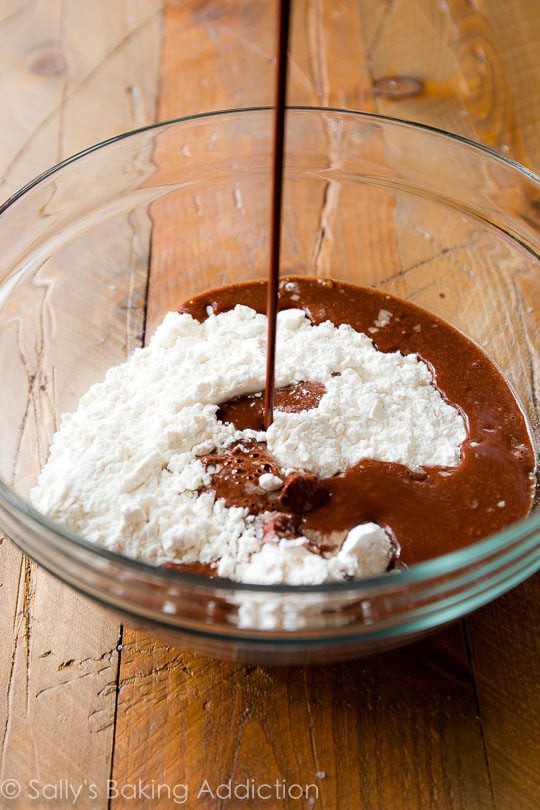 pouring chocolate mixture into flour mixture in a glass bowl
