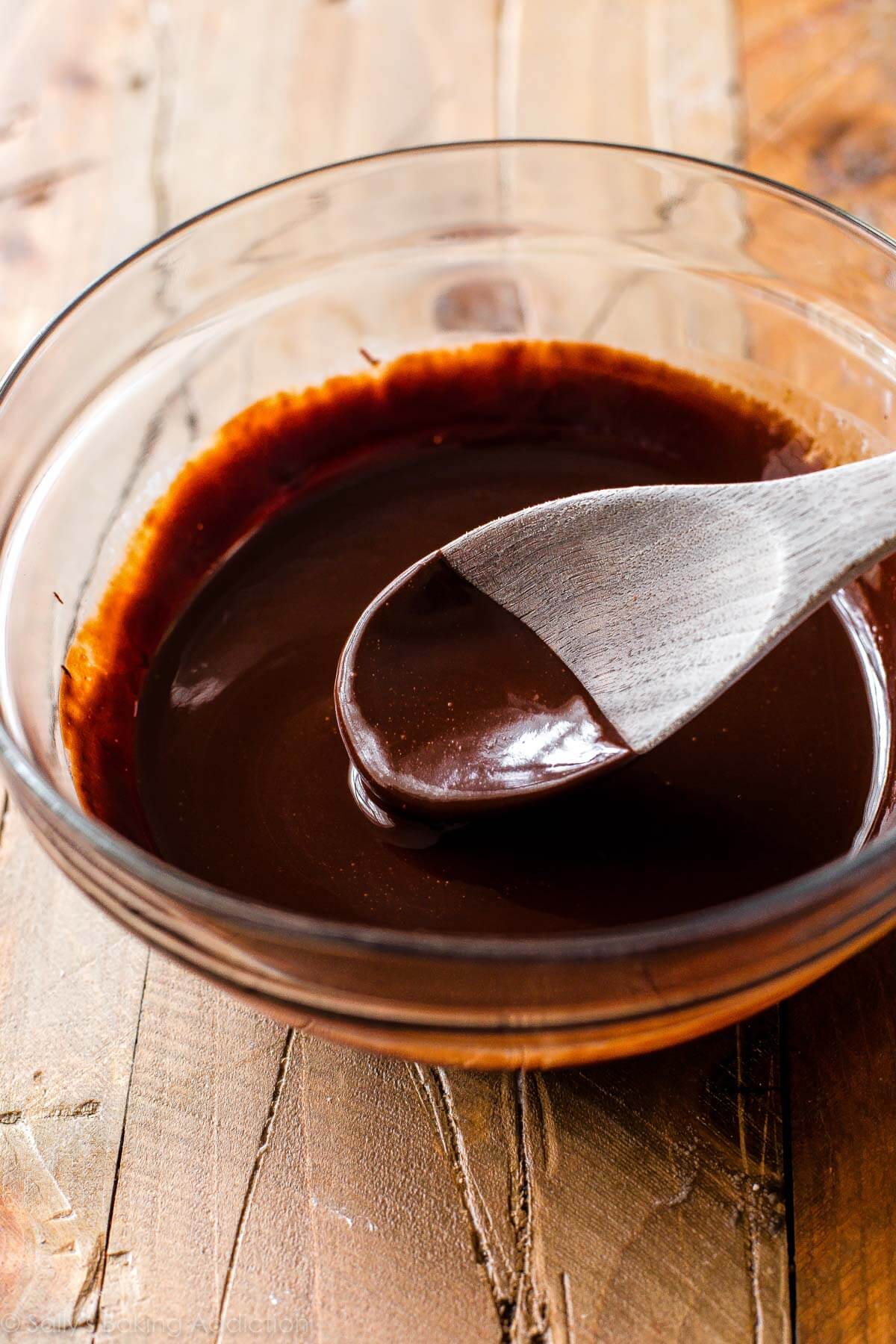 melted chocolate in a glass bowl with a wood spoon