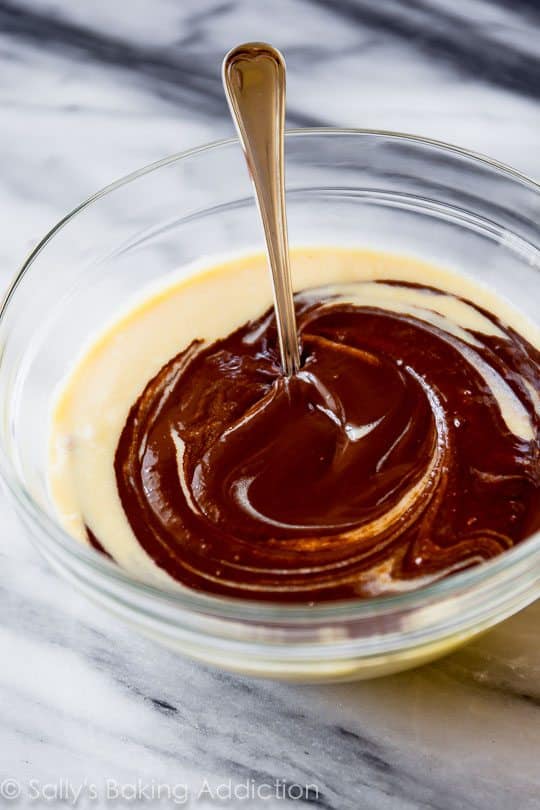 swirling melted chocolate into yellow cake batter in a glass bowl with a spoon