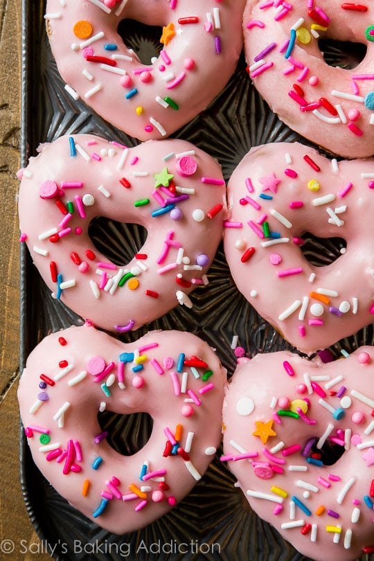 heart shaped donuts topped with pink glaze and sprinkles on a baking sheet