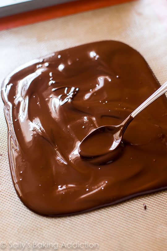 spreading melted chocolate onto a silpat baking mat with a spoon