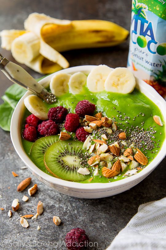 green smoothie in a bowl topped with kiwi, almonds, chia seeds, banana slices and raspberries