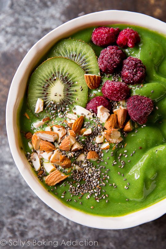 green smoothie in a bowl topped with kiwi, almonds, chia seeds, and raspberries