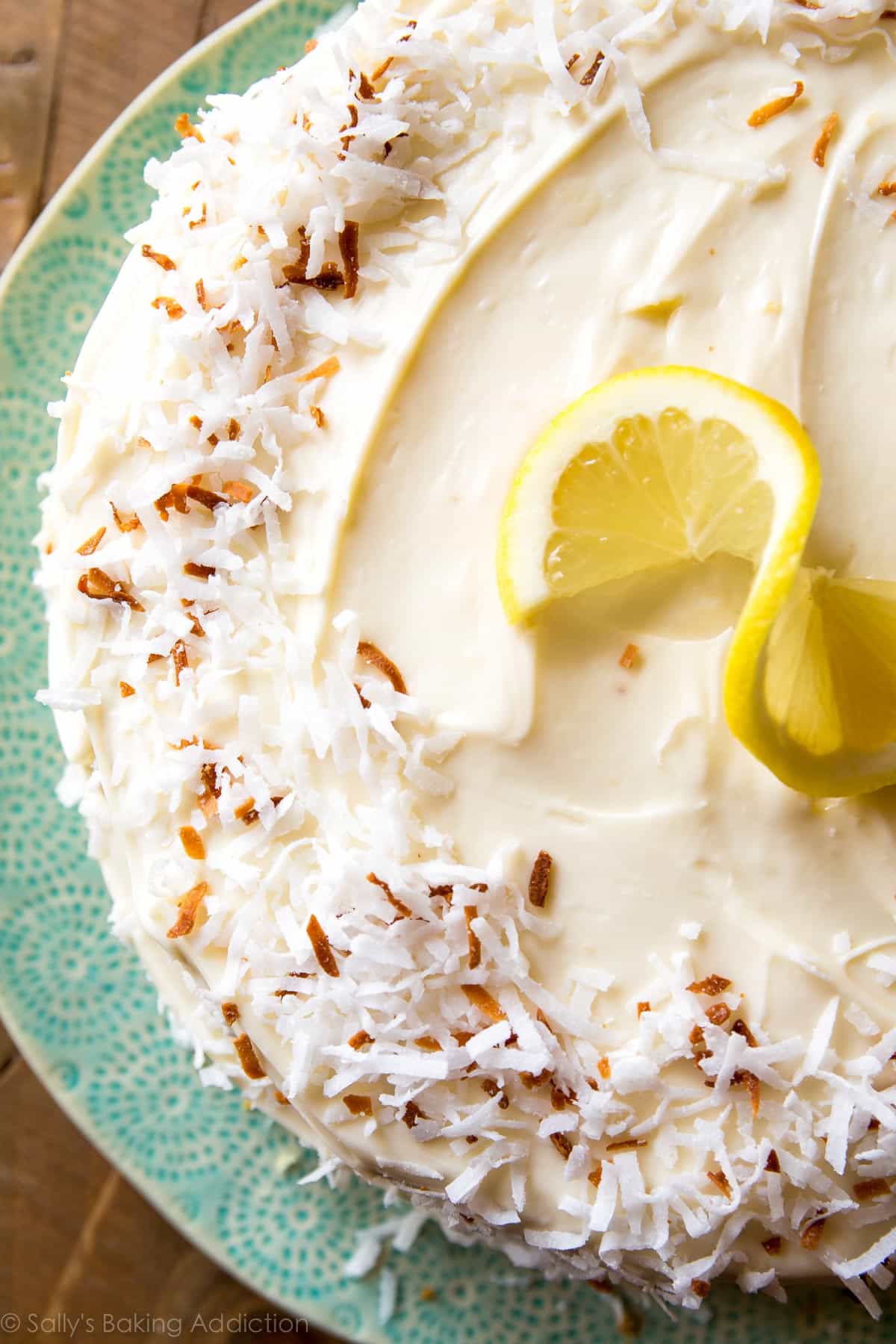 overhead image of lemon coconut cake garnished with coconut and a lemon slice on a teal plate