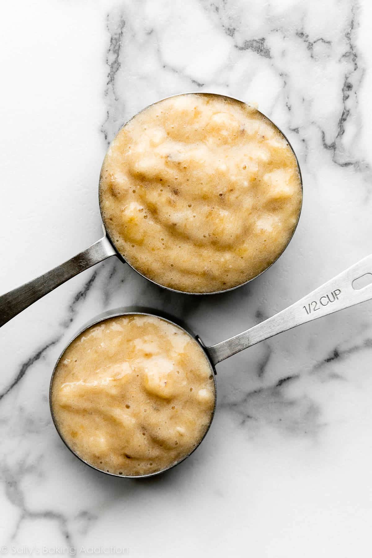 two measuring cups of mashed banana on marble counter.