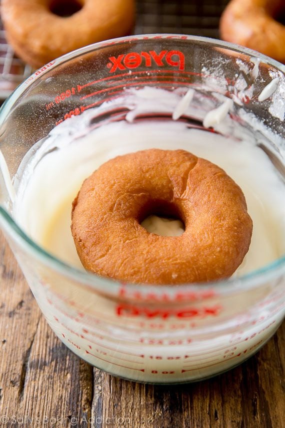 doughnut dipped in a glass measuring cup filled with glaze