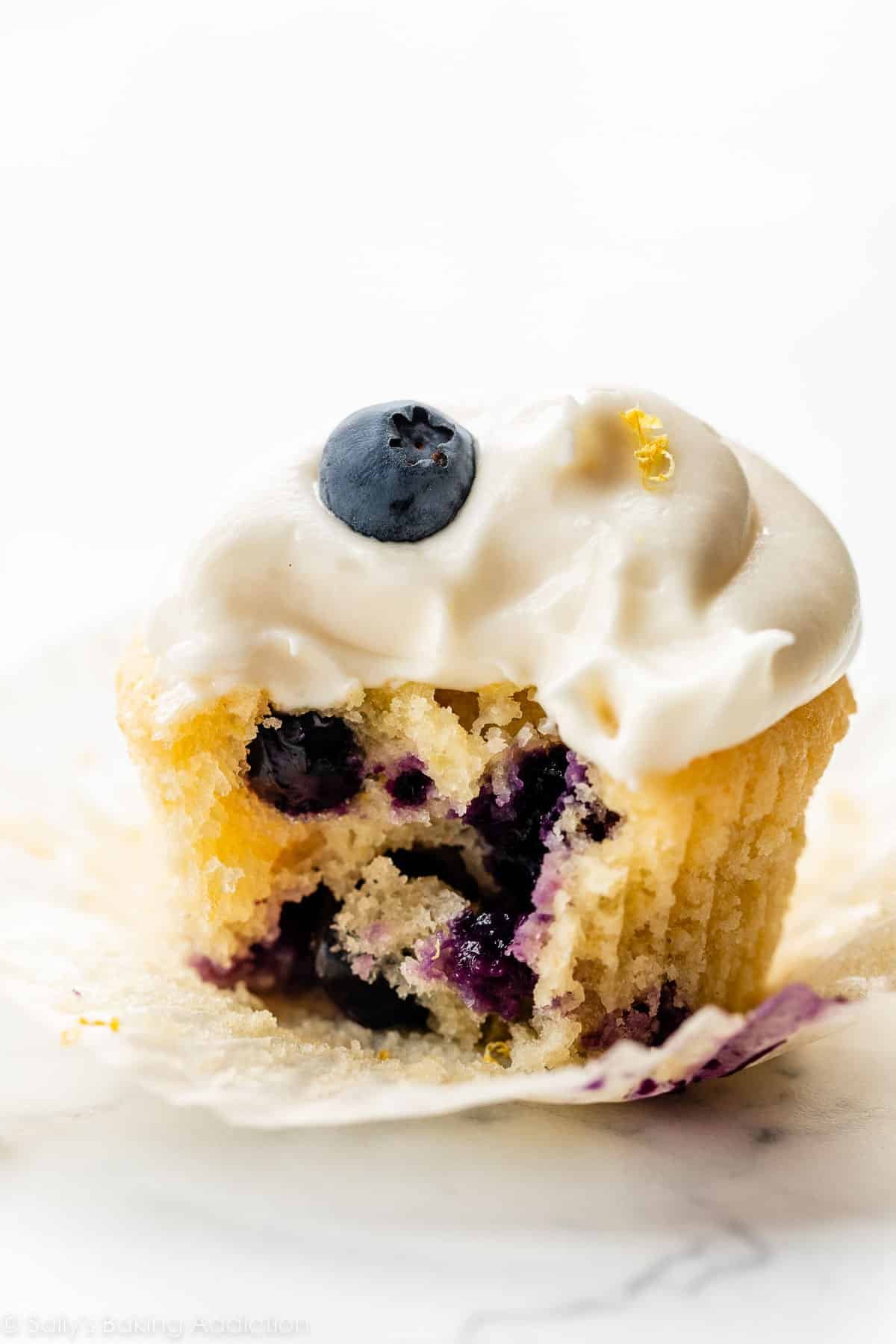 bite taken out of a lemon blueberry cupcake with cream cheese frosting.