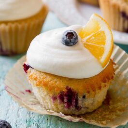 lemon blueberry cupcakes topped with cream cheese frosting, a blueberry, and lemon wedge