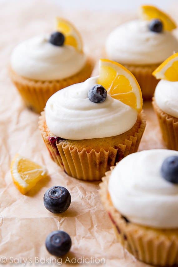 lemon blueberry cupcakes topped with cream cheese frosting, a blueberry, and lemon wedge