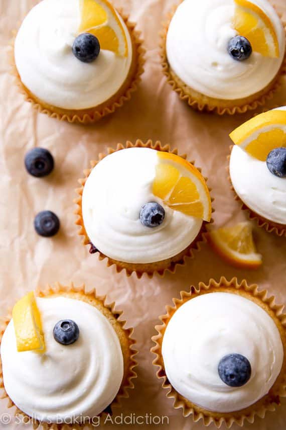 overhead image of lemon blueberry cupcakes topped with cream cheese frosting, a blueberry, and lemon wedge