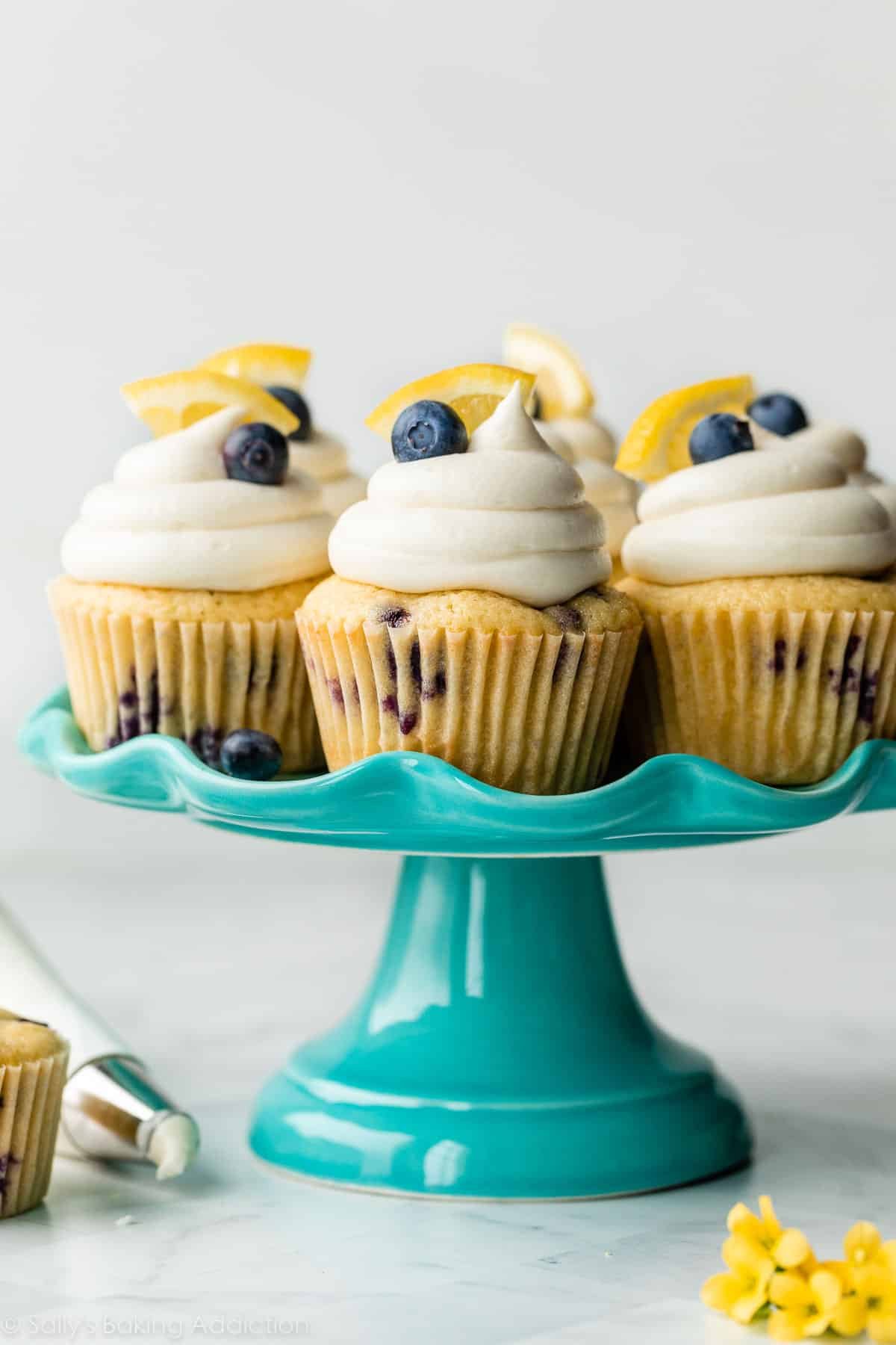 lemon blueberry cupcakes with cream cheese frosting on blue cake stand.