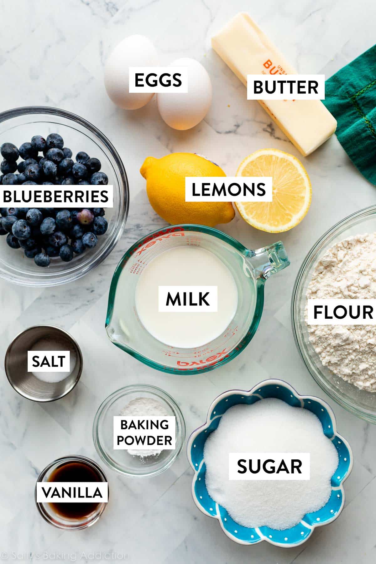 lemons, milk, flour, sugar, baking powder, butter, blueberries, and other ingredients on counter.
