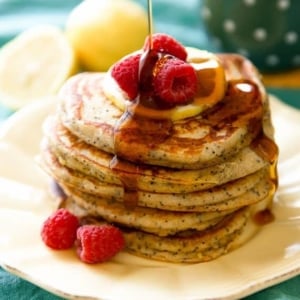 stack of lemon poppy seed pancakes with maple syrup on a cream plate